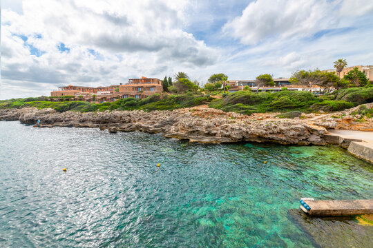 The rocky coastline and turquoise waters of the Mediterranean Sea at the whitewashed town of Binibeca Vell, on the Balearic island of Menorca, Spain.