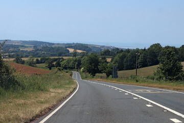 Downhill on an empty road in Somerset, England. Lush green rolling hills can be seen in the...