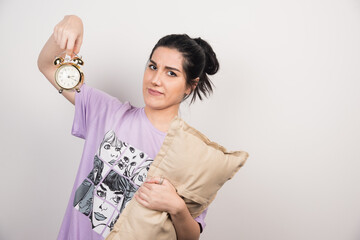 Young woman holding alarm clock and cushion on white background