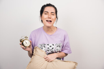 Sad woman holding alarm clock and cushion on white background