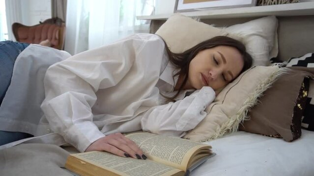Slow Motion young caucasian girl asleep while reading a book on the bed 