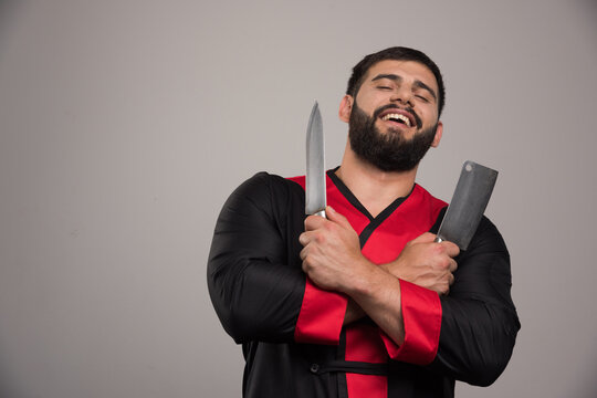 Smiling Man Holding Two Knifes On Dark Background