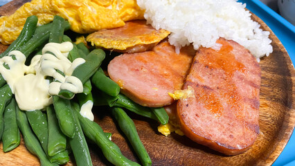 スパムハムと茹でたインゲン豆とオムレツのワンプレートご飯。木製の皿とブルーのトレイで朝食