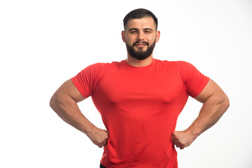 Fototapeta premium Sportive man in red shirt demonstrating his arm muscles and looks confident