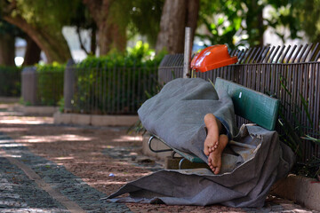Homeless covered with blanket sleeping on a bench at Matriz Square (Praça da Matriz), Porto...