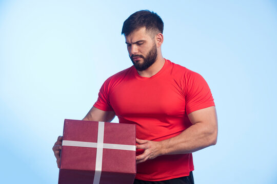 Man In Red Shirt Holding A Big Gift Box And Looks Serious