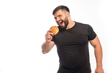 Sportive man in black shirt holding a doughnut and eating