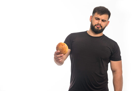 Sportive man in black shirt holding a doughnut and refusing