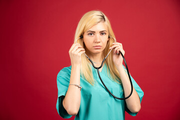 Female nurse in uniform using stethoscope on red background