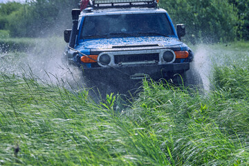 Obraz na płótnie Canvas Water splashes during off-road racing. Blue SUV drive through a dangerous water barrier at high speed. A sports car with all-wheel drive is racing at high speed. The concept of adventure and travel