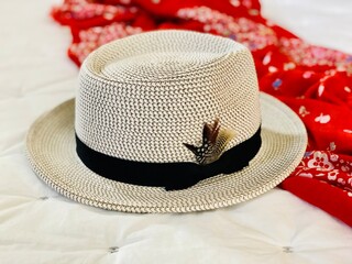 Fashion accessories woman’s brimmed fedora hat and bright orange scarf laid out on a white quilt