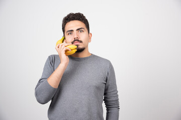 Serious male talking with banana on gray background