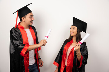 Fresh graduates in gown posing with diploma on white background