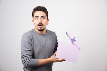 Shocking man with an opened purple box over a white wall