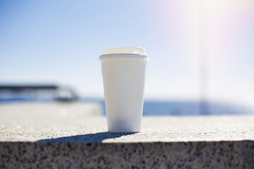 
White cup of coffee on sea background at sunset time