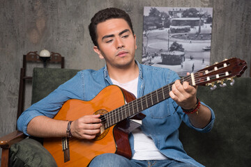Young musician playing the guitar and sitting on sofa