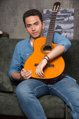 Musician holding a beautiful guitar and sitting on sofa