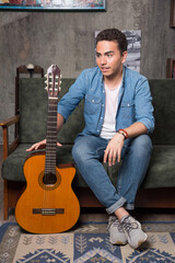 Young guitar player holding a beautiful guitar and sitting on sofa
