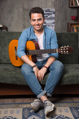Young musician holding a beautiful guitar and sitting on sofa