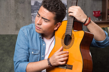 Man with closed eyes holding a beautiful guitar and sitting on sofa