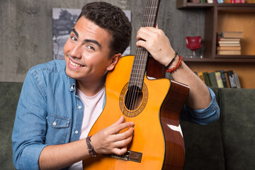 Cheerful man showing a beautiful guitar and sitting on sofa