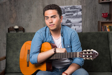 Young man sitting on sofa with a beautiful guitar