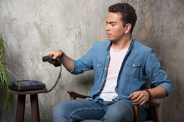 Disgruntled man holding handset and sitting on chair