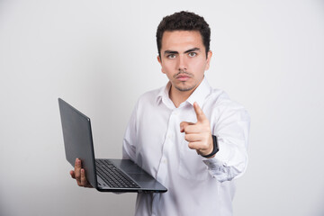 Businessman with laptop pointing at camera on white background