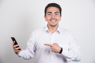 Smiling businessman pointing at telephone on white background