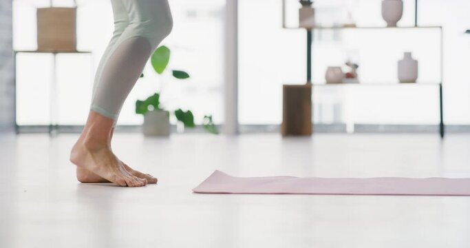 A woman rolls out a yoga mat on the floor in a yoga fitness training room. Active and fit barefoot woman prepares for a home workout to live a healthy lifestyle with a balanced mind and body at home