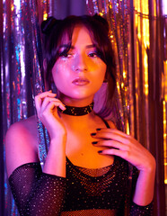 portrait of a young woman at a neon party placed in front of a Metallic Party Rain Curtain. Creative make up and hair. Perfect nails