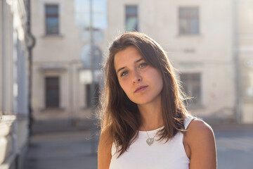 Portrait of a cute brunette girl on the background of a city house on a sunny summer day - obrazy, fototapety, plakaty