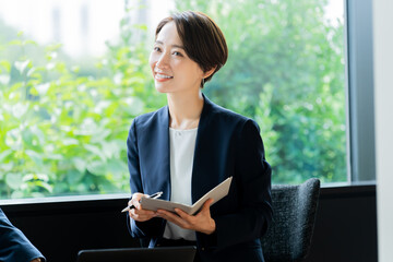 オフィスで手帳を持ち話をするスーツを着た日本人女性