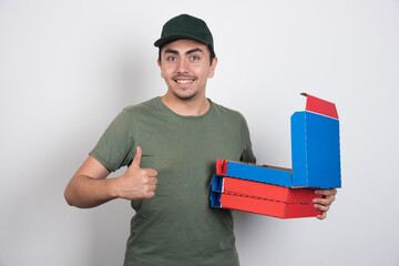 Deliveryman showing thumbs up and carrying pizza boxes on white background