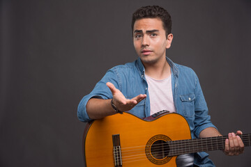 Young man with guitar looking puzzled on dark background