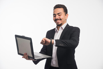 A businessman in dress code holding a laptop and pointing time