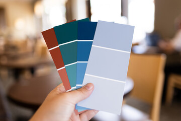 One human hand holding a few paint sample swatches getting ready to remodel a house choosing paint interior design