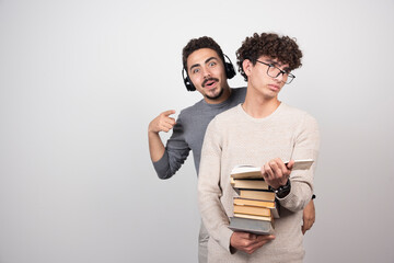 Young guy carrying a lot of books and another guy listening music in headphones