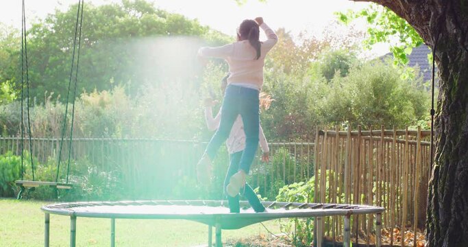 Happy little girls jumping on a trampoline on a sunny day. Two energetic and excited young siblings playing and having fun together while bouncing with joy on a net in the backyard with lens flare