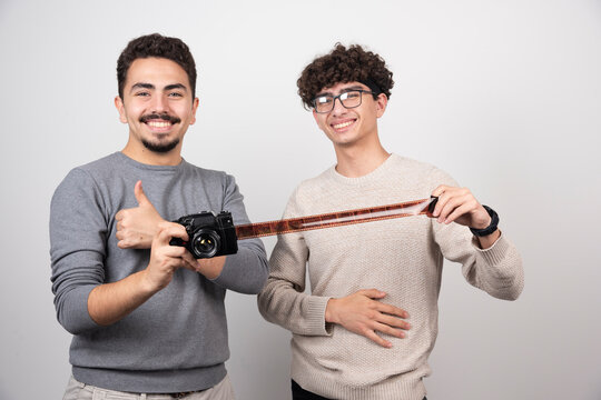 Two young men holding a camera and showing a thumb up