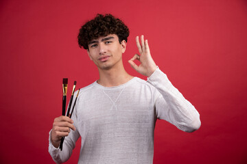 Male artist with brushes giving ok sign