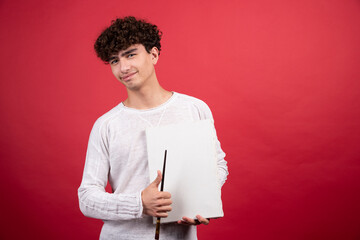Young boy holding empty canvas and brush on red background