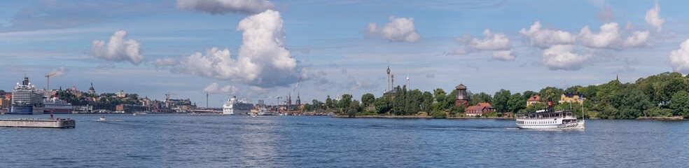 Obraz premium Panorama view at the bay Saltsjön an old steam boat leaving for the archipelago, large cruise ships at the pier Masthamnen and the old town Gamla Stan with cumulus clouds a sunny summer day Stockholm