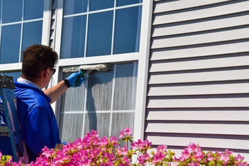 A man is seen wiping soap off of an exterior window he is cleaning with a squeegee
