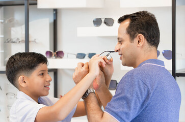 Indian father and son choosing eyeglasses in optics store, Family buy glasses