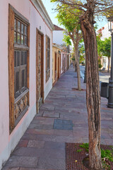 Fototapeta na wymiar City view paved sidewalk with trees and residential houses or buildings on a quiet street in Santa Cruz, La Palma, Spain. Historical spanish and colonial architecture and famous tourism destination