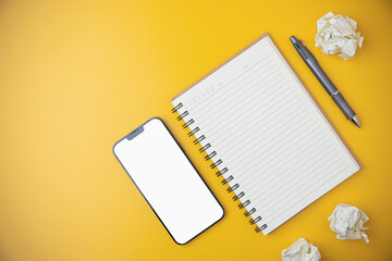 Flat lay of office yellow desk with a smartphone. Top view blank notebook with a pen on yellow table with copy space. Business, technology, study, and learning concept.