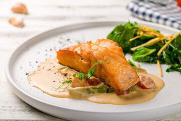 Salmon steak on the grill with spinach on white plate on white wooden table macro close up