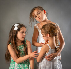 Portrait three sisters mixed race oldest bridesmaid flower girl looks at camera while hugging little sister
- 515968625