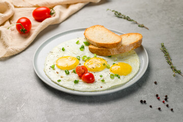 Fototapeta na wymiar Fried eggs with tomatoes, toasts and green onion on grey table